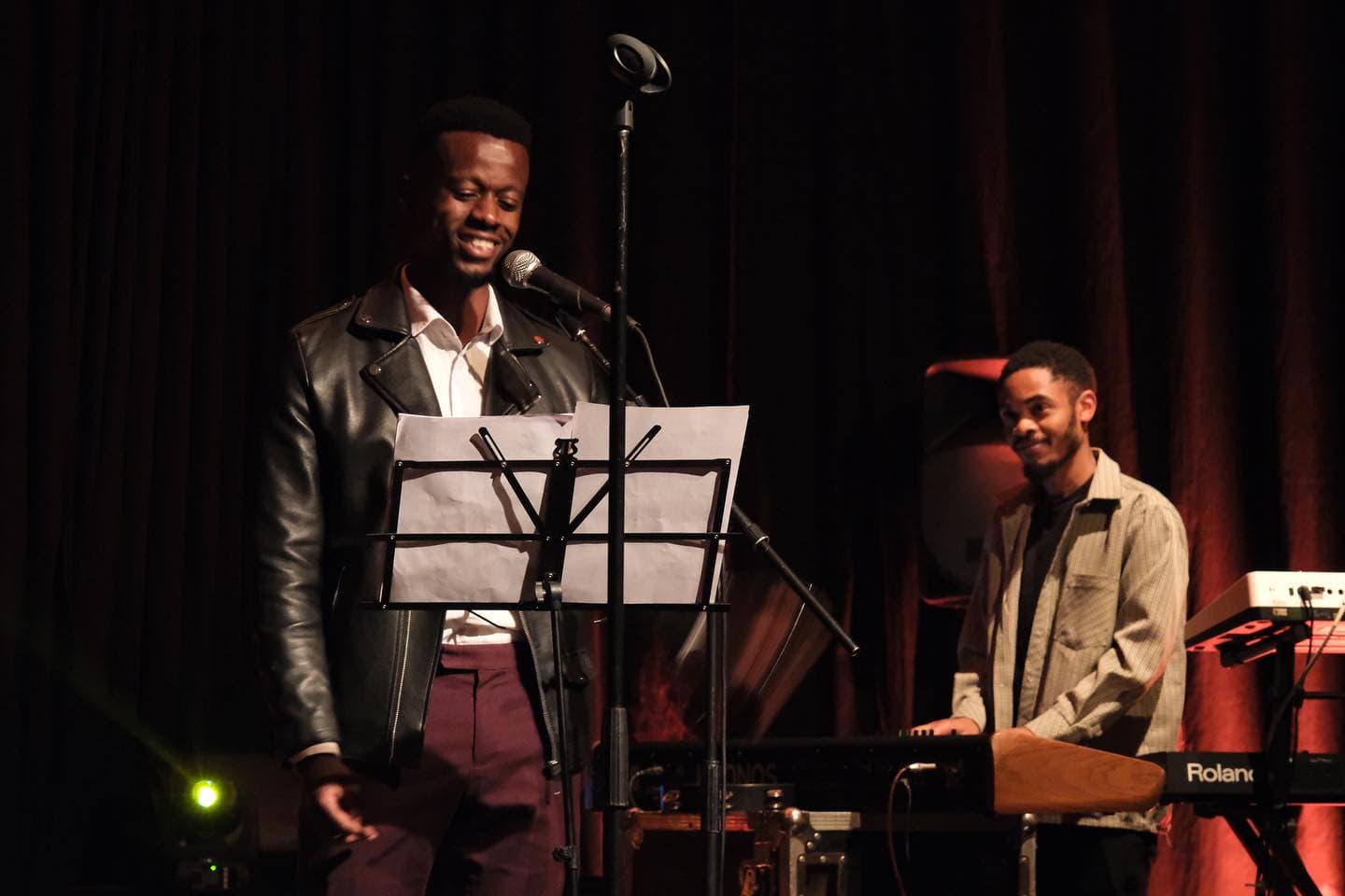 Young male vocalist smiling with music stand and live keyboard accompanist on stage